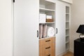 White built-in wardrobe with sliding doors and open middle shelves holding towels and pillows, plus a light wood chest of drawers below.