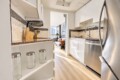 Bright, modern kitchen with white cabinets, granite counters, stainless appliances, and a doorway to a living room.