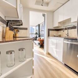 Bright, modern kitchen with white cabinets, granite counters, stainless appliances, and a doorway to a living room.