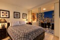 Modern bedroom with geometric duvet, three framed pictures, and a balcony overlooking city lights at night.