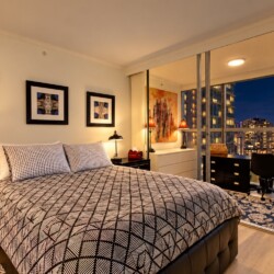 Modern bedroom with geometric duvet, three framed pictures, and a balcony overlooking city lights at night.