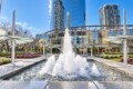Modern glass office building with a large central fountain and landscaped plaza in front.