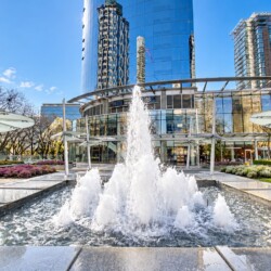 Modern glass office building with a large central fountain and landscaped plaza in front.