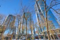 Low-angle view of tall glass skyscrapers reflecting a blue sky, framed by leafless trees in an urban plaza.