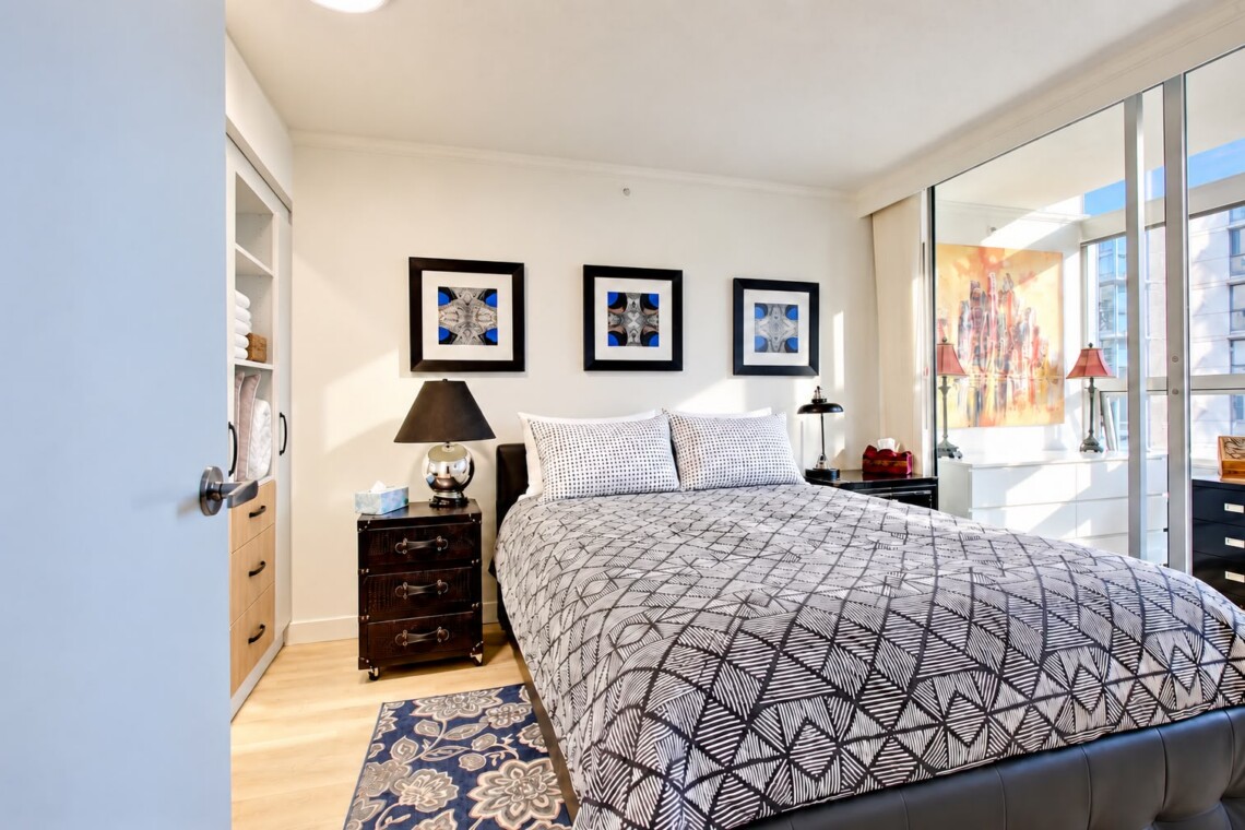Modern bedroom with a patterned quilt, two nightstands, and three framed geometric art pieces above the bed.