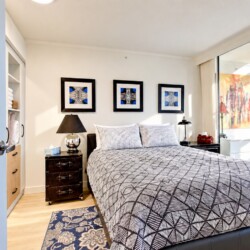 Modern bedroom with a patterned quilt, two nightstands, and three framed geometric art pieces above the bed.