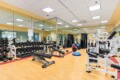 Well-equipped gym with dumbbell racks, benches, and weight machines in a bright, mirrored room with yellow accents.