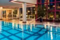 Indoor swimming pool in a fitness center, with the gym visible through glass walls in the background.